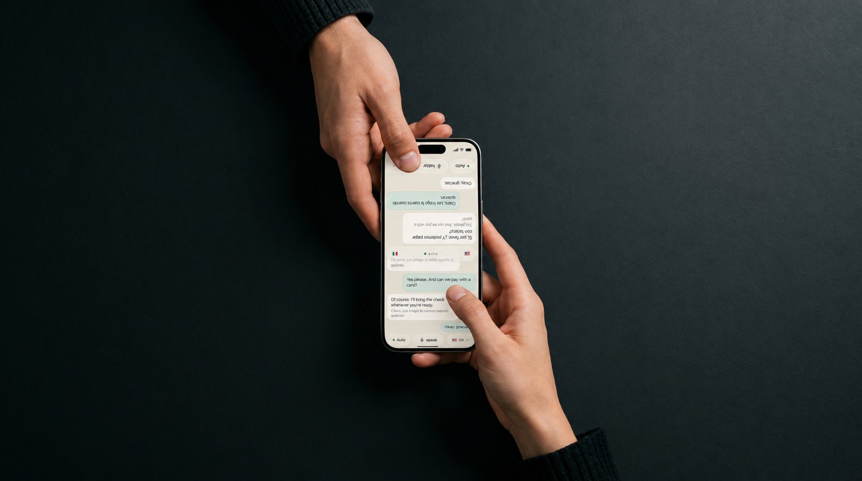 Two hands over a dark table, one iPhone between them: the near half of the screen in English, the far half flipped and in Spanish